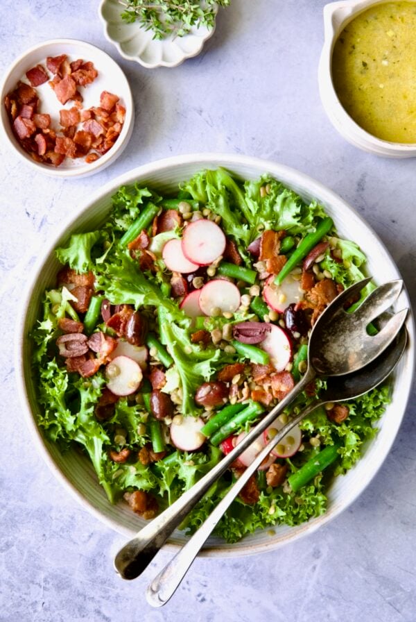 French Lentil Salad in white serving bowl with serving utensils.