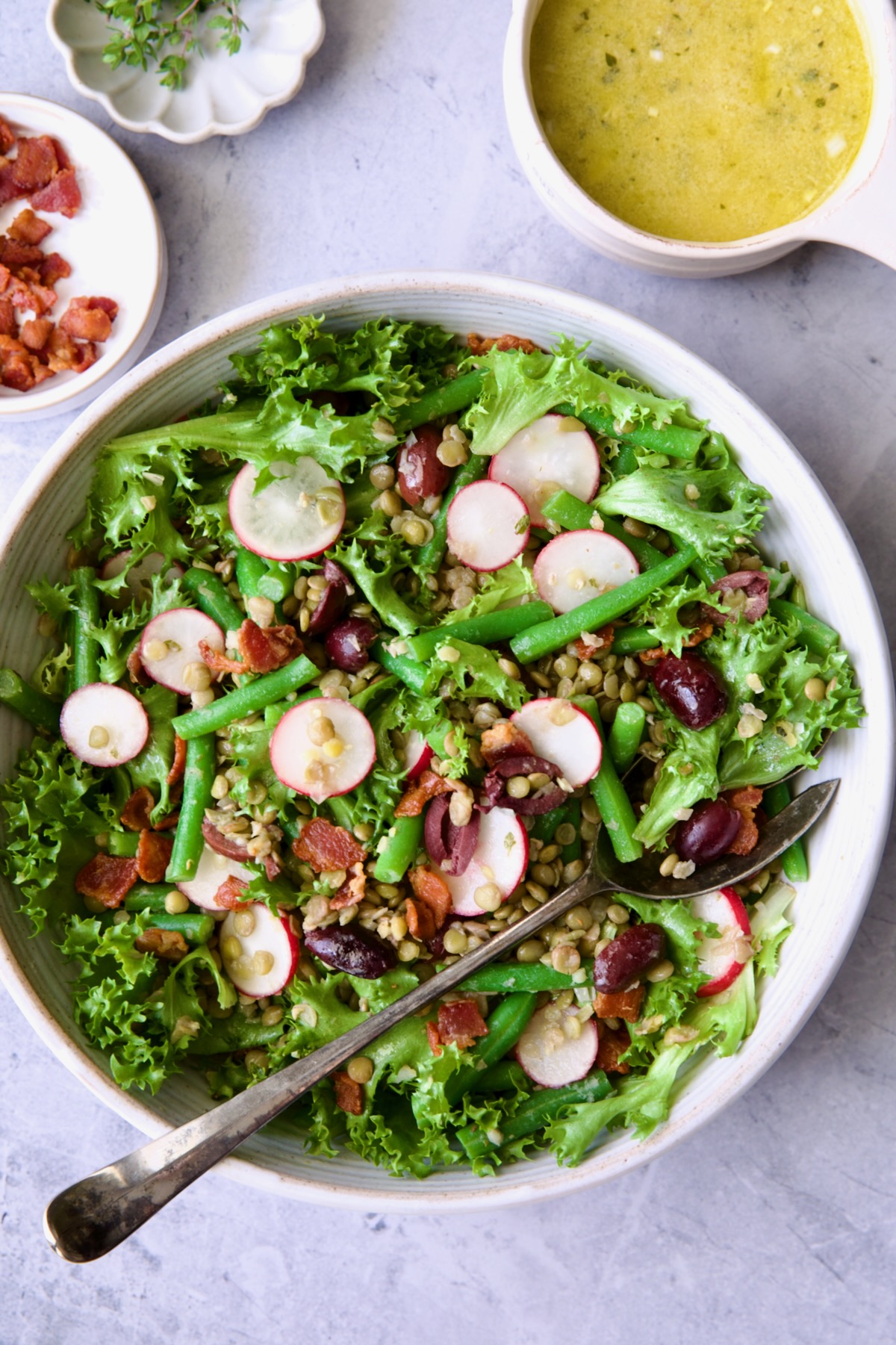 French Lentil Salad in white serving bowl with serving utensils.