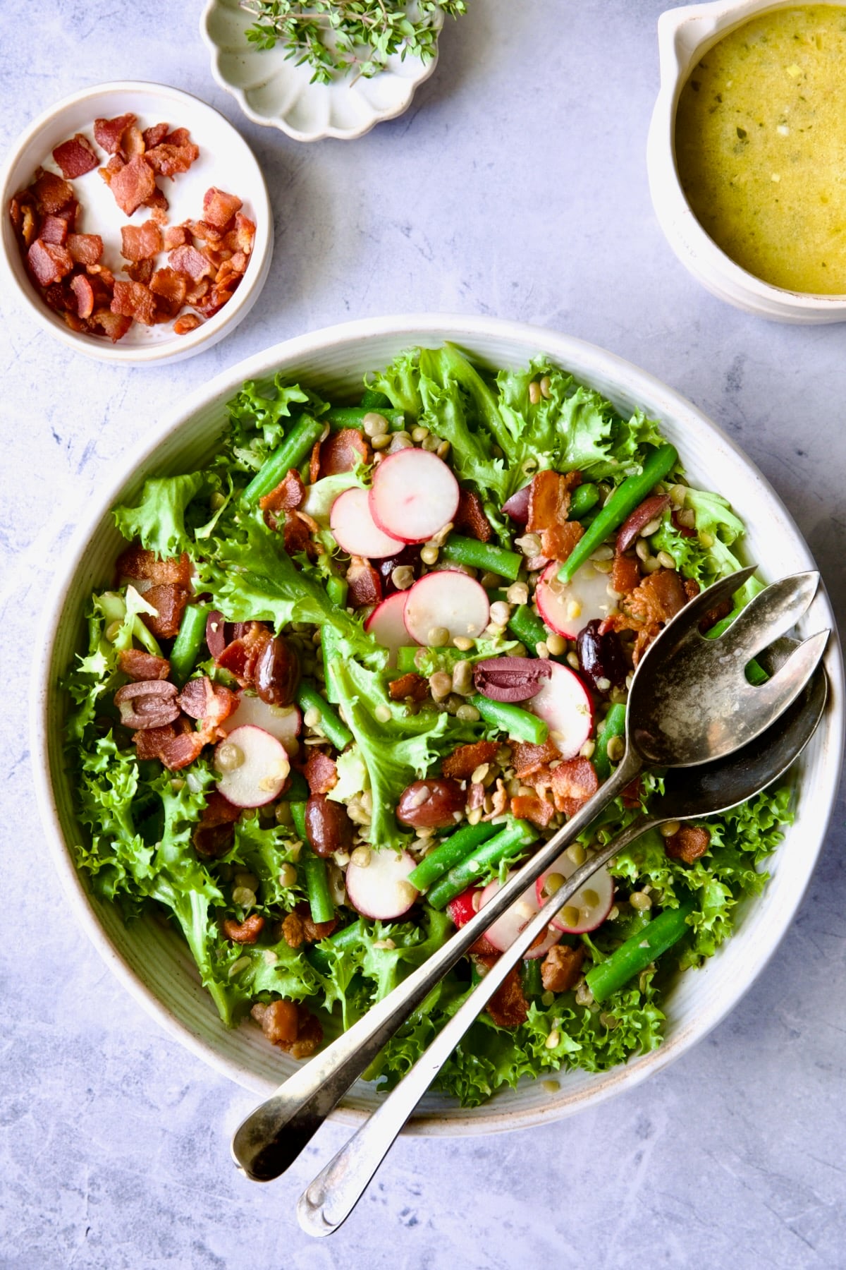 French Lentil Salad in white serving bowl with serving utensils.