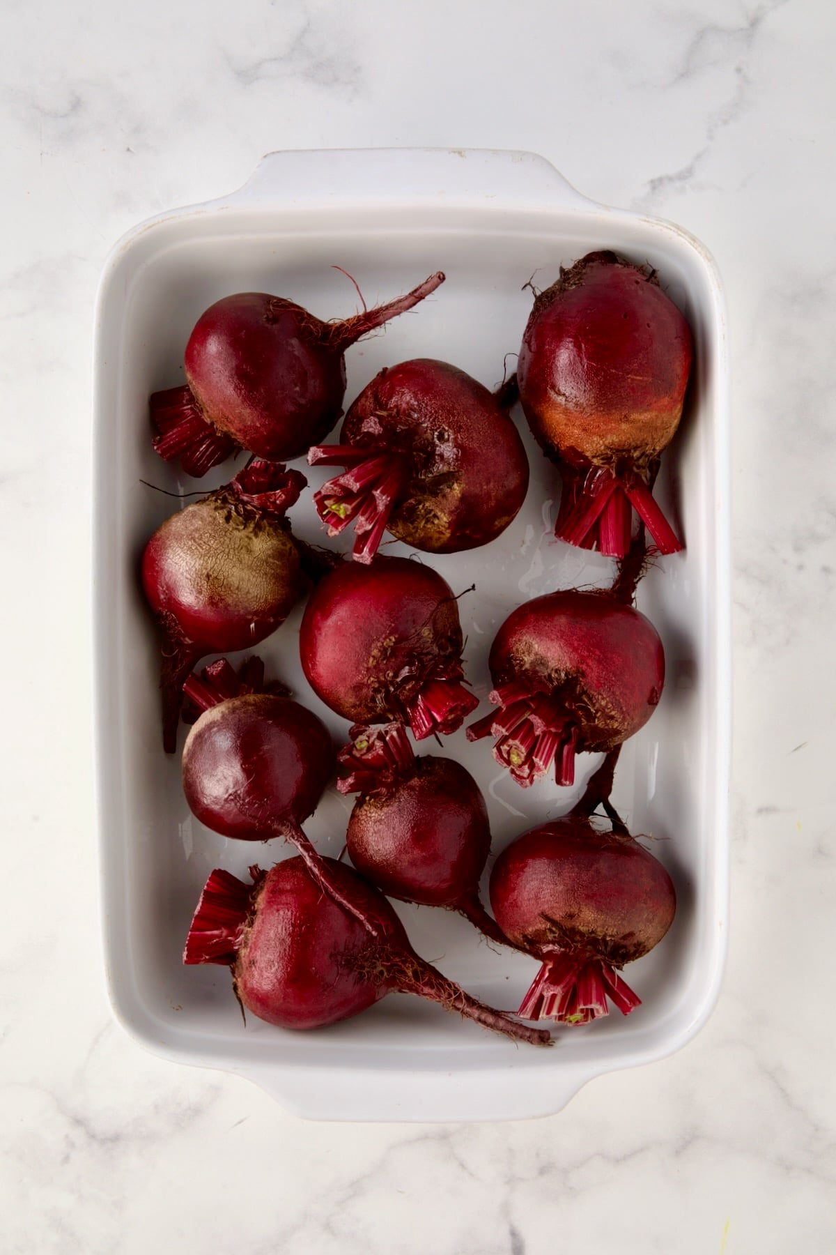 Uncooked beets in white rectangular baking dish.