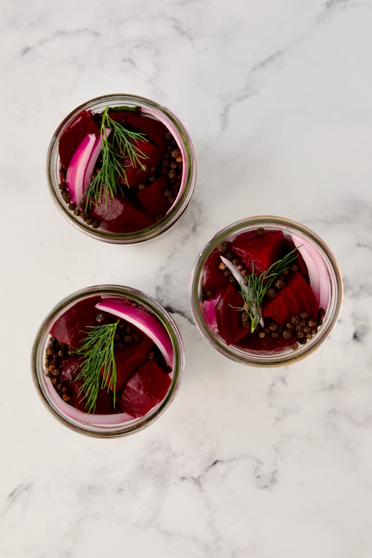 Three pint jars packed with beets, red onion, dill and peppercorns.