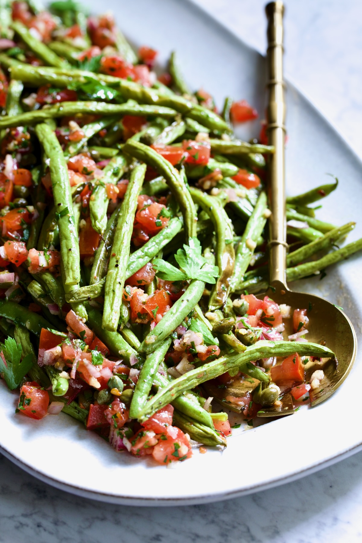Roasted Green Beans with Tomato Caper Relish on oval white platter with serving spoon.