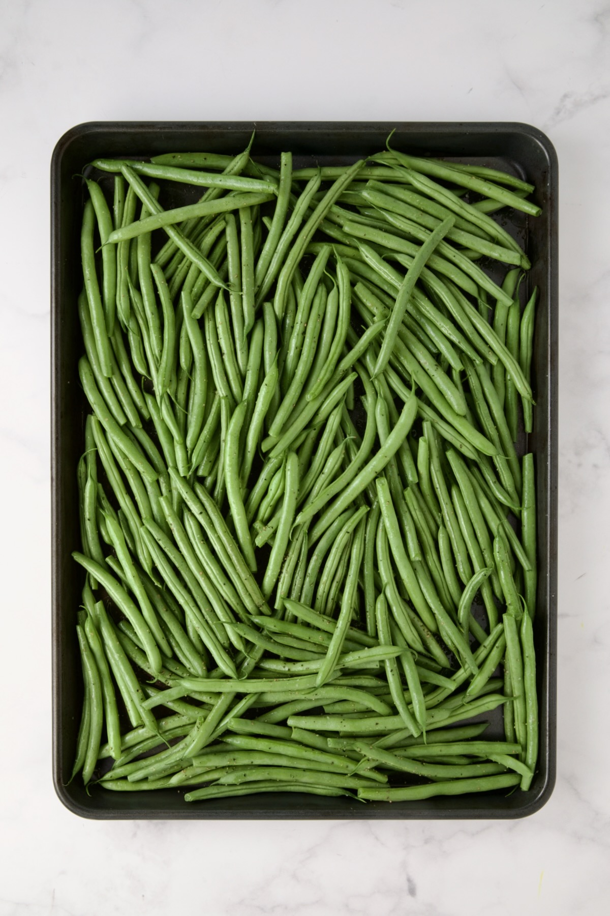 Fresh green beans on rimmed sheet pan before being roasting.