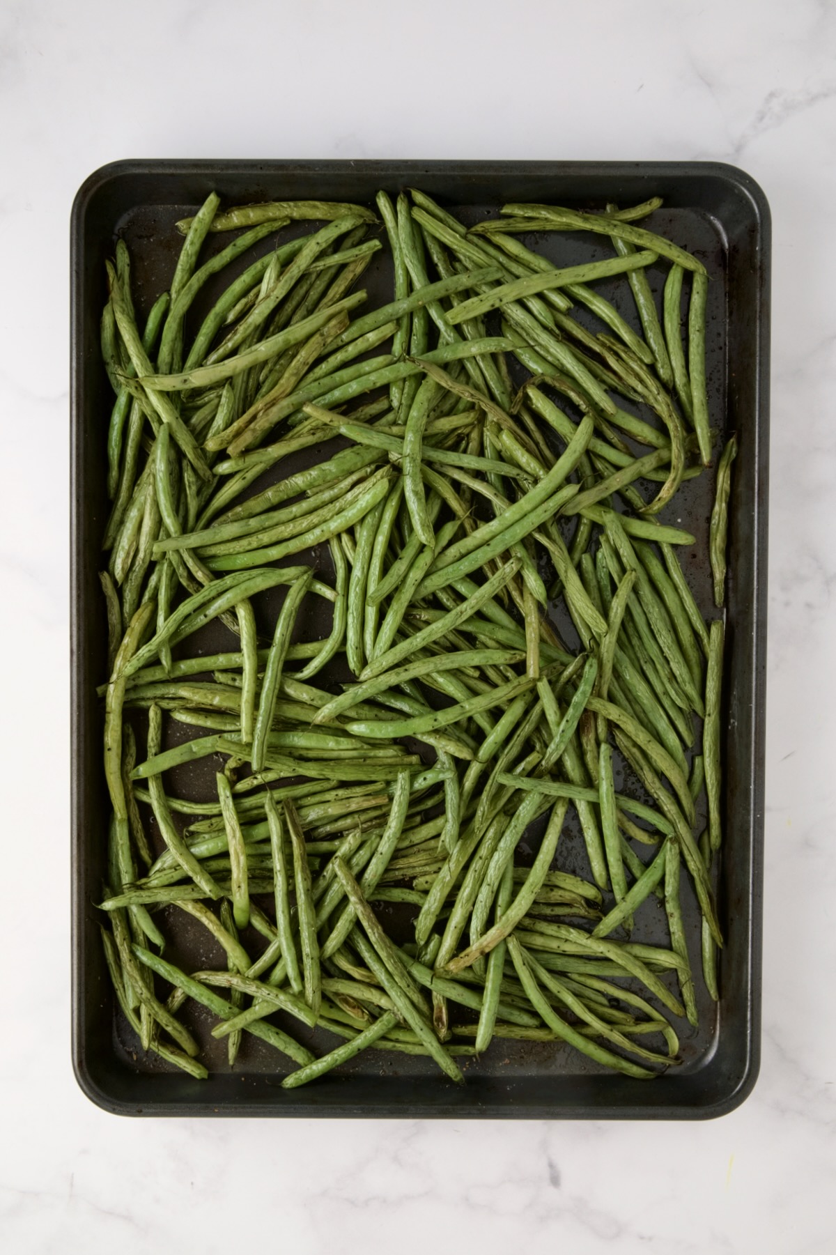 Roasted green beans on rimmed sheet pan.