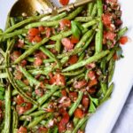 Roasted Green Beans with Tomato Caper Relish on oval white platter with serving spoon.