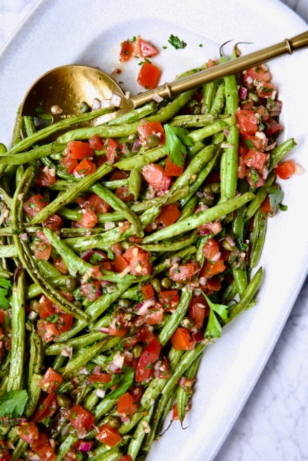 Roasted Green Beans with Tomato Caper Relish on oval white platter with serving spoon.