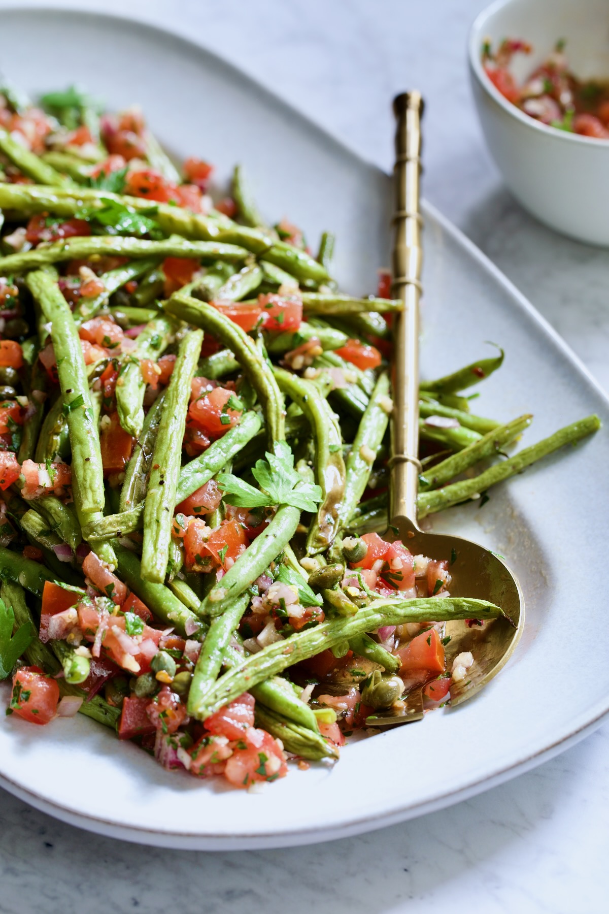 Roasted Green Beans with Tomato Caper Relish on oval white platter with serving spoon.