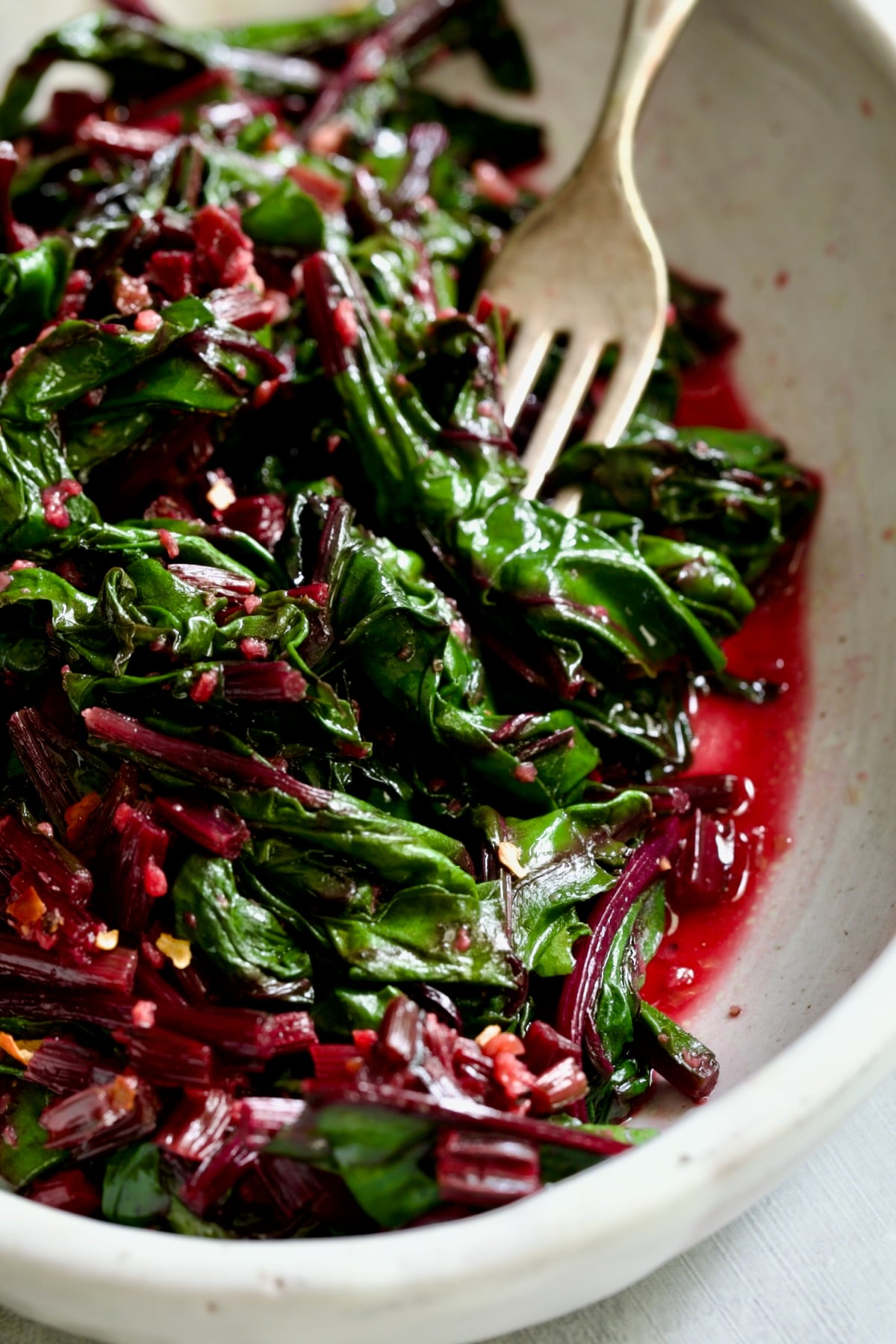 Sauteed Beet Greens in oval white serving bowl with fork.