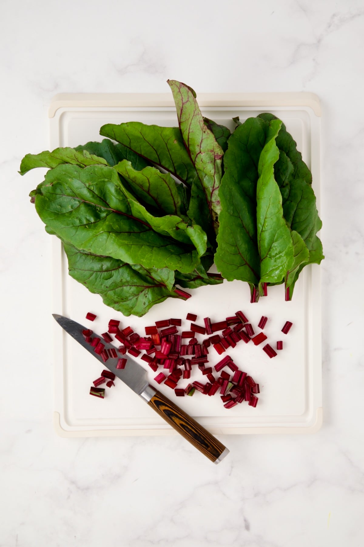 Beet greens and chopped stems on white cutting board.