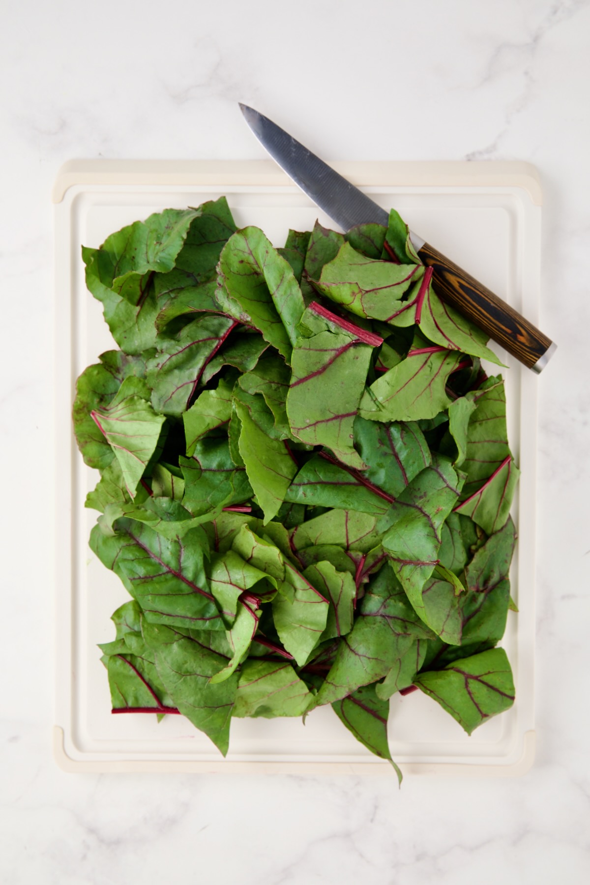Coarsely chopped beet greens on white cutting board.