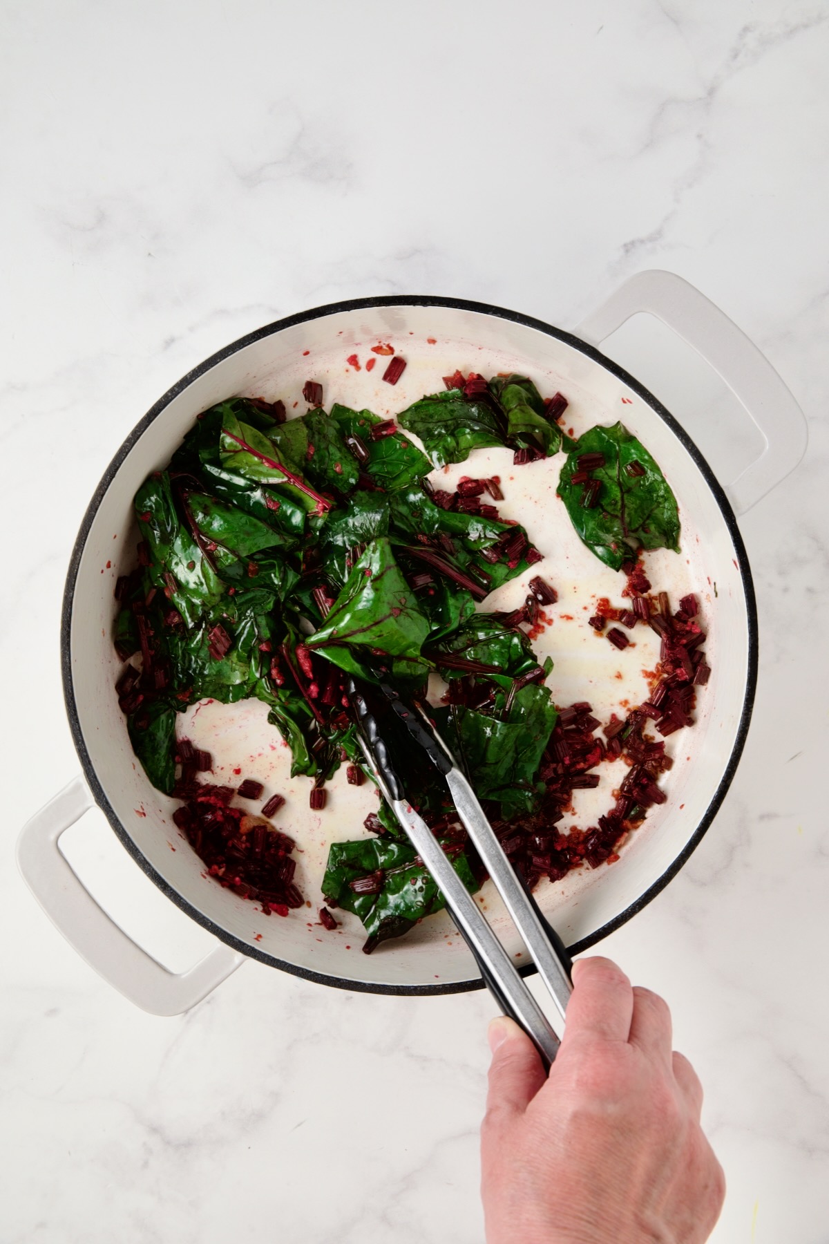 Wilted beet greens in white enamel cast iron skillet.