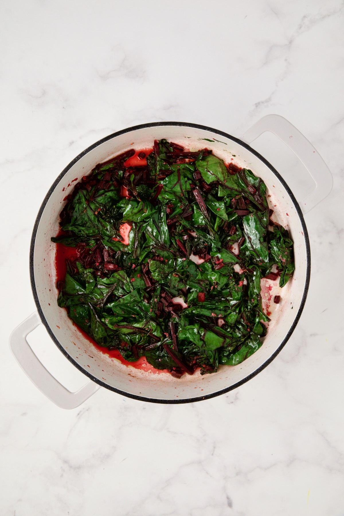 Cooked beet greens in white enamel cast iron skillet.
