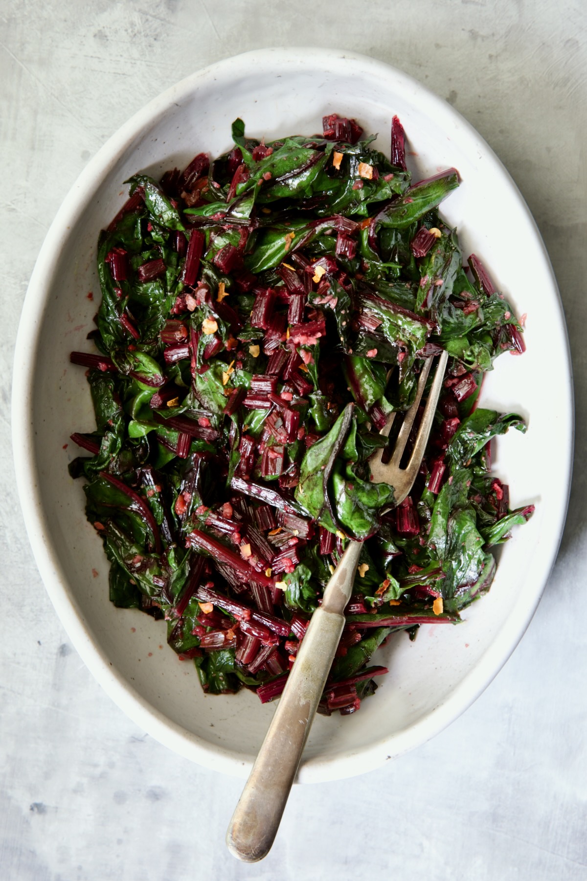 Sauteed Beet Greens in oval white serving bowl with fork.