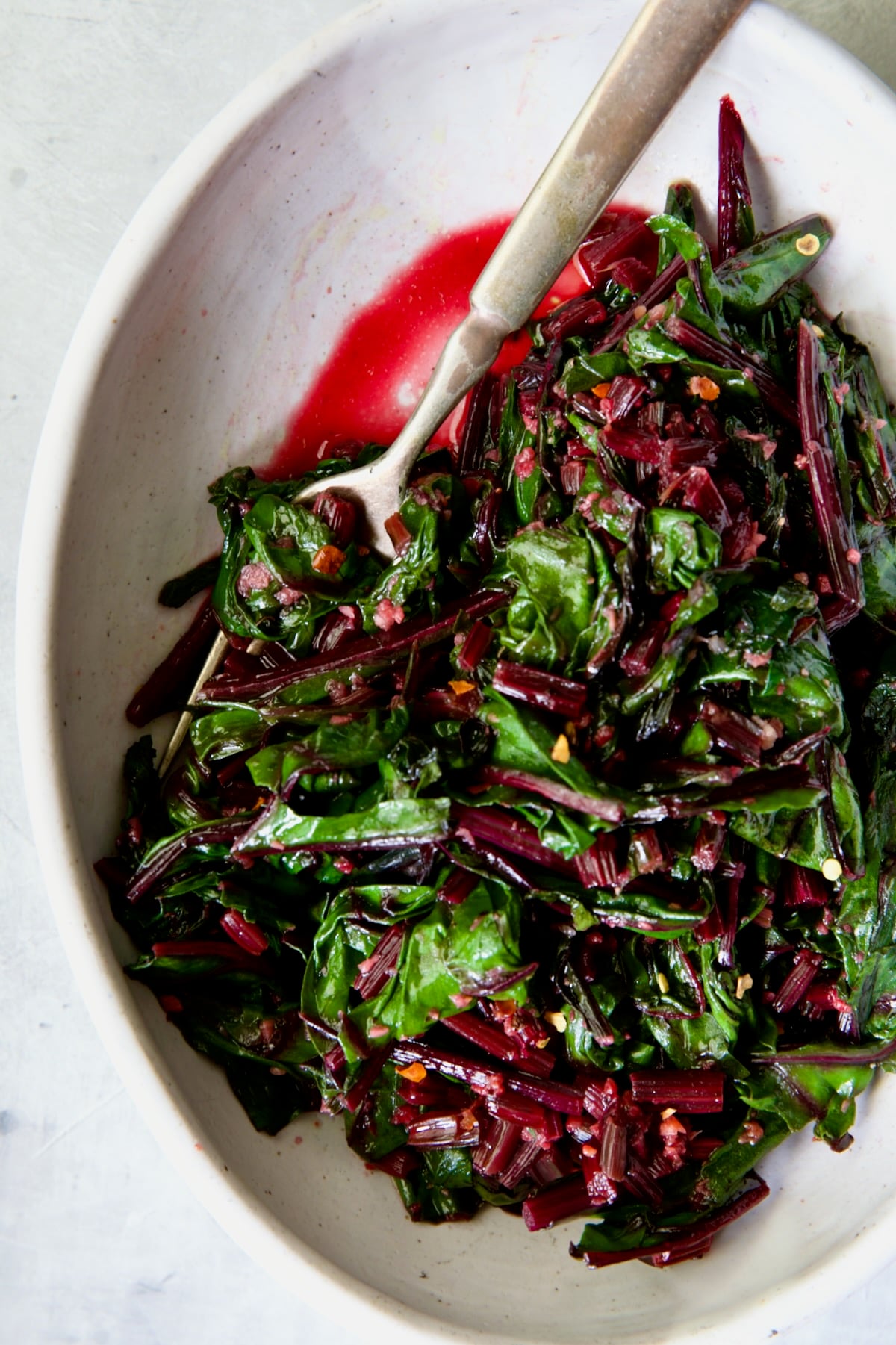 Sauteed Beet Greens in oval white serving bowl with fork.