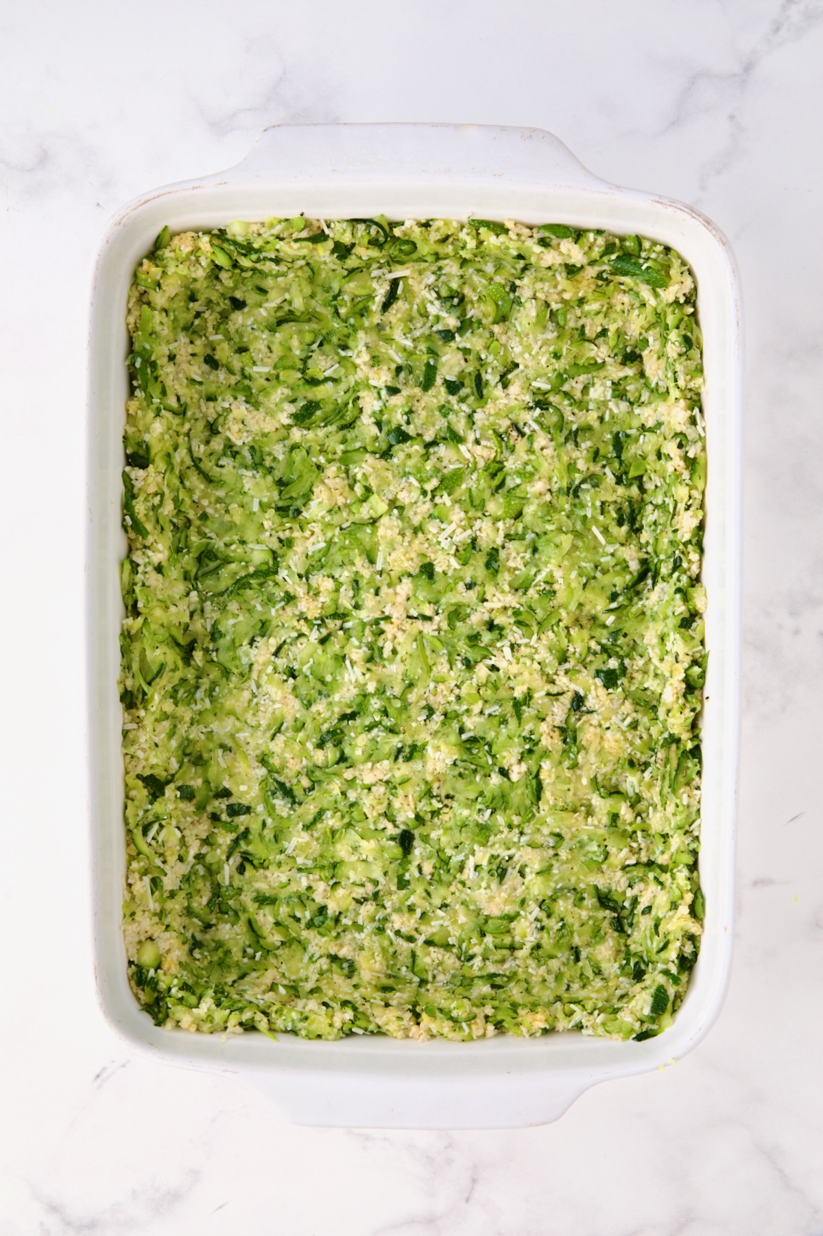 Zucchini crust in white rectangular baking dish before being baked.