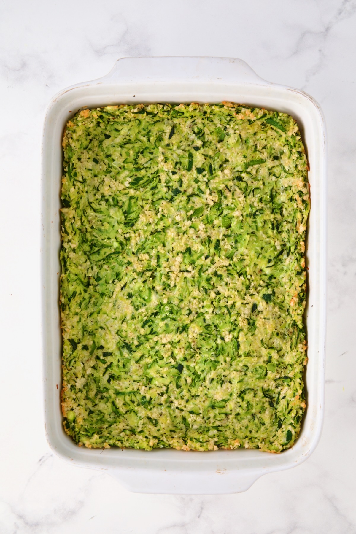 Zucchini crust in white rectangular baking dish after being baked.