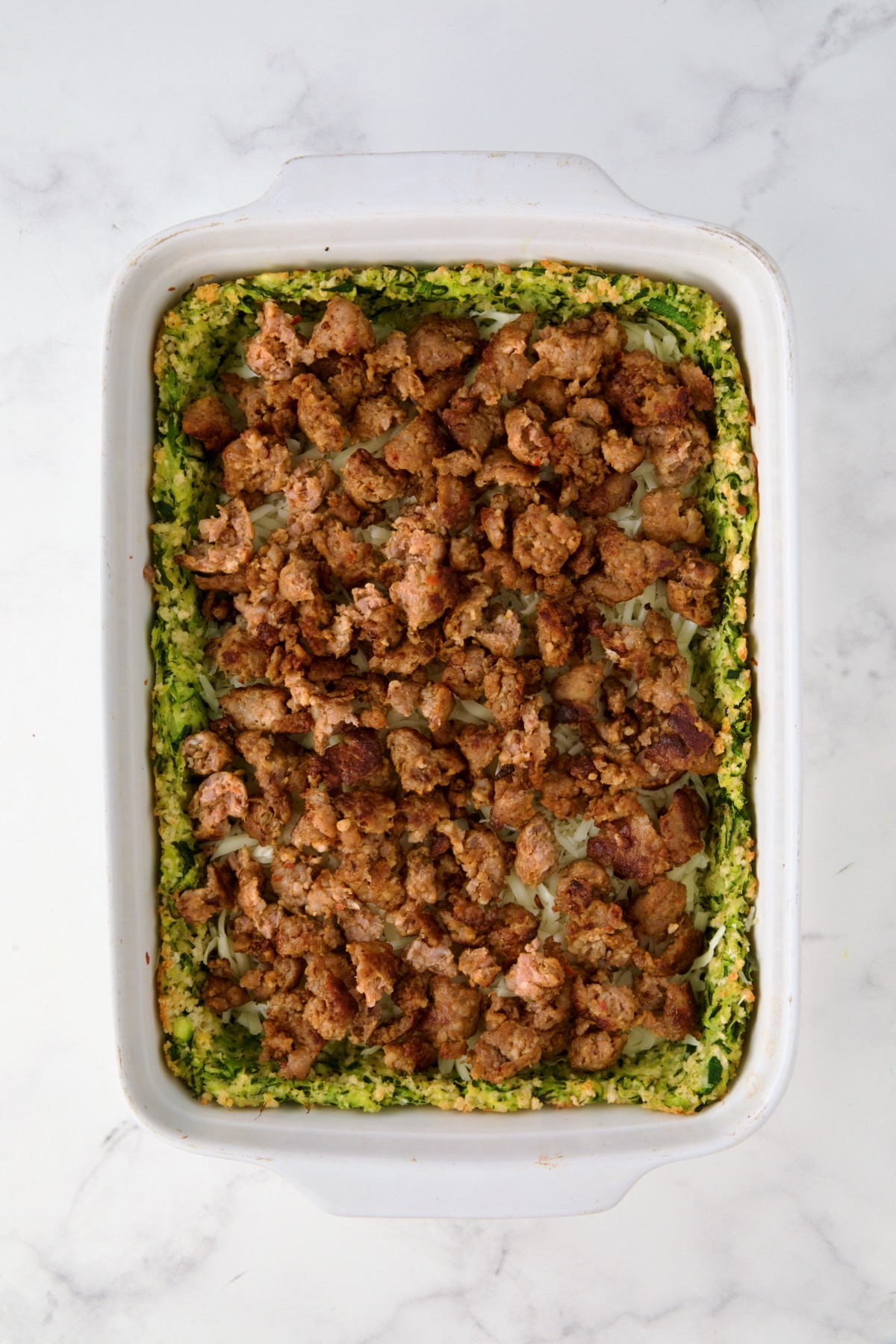 Italian sausage placed over cheese layer in white rectangular baking dish.
