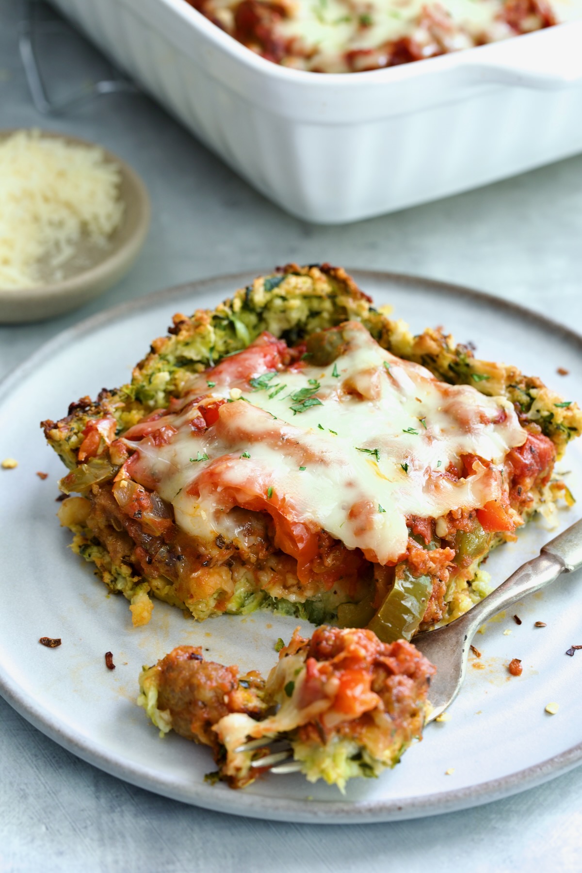 Piece of Zucchini Pizza Casserole on small plate with a piece on a fork.