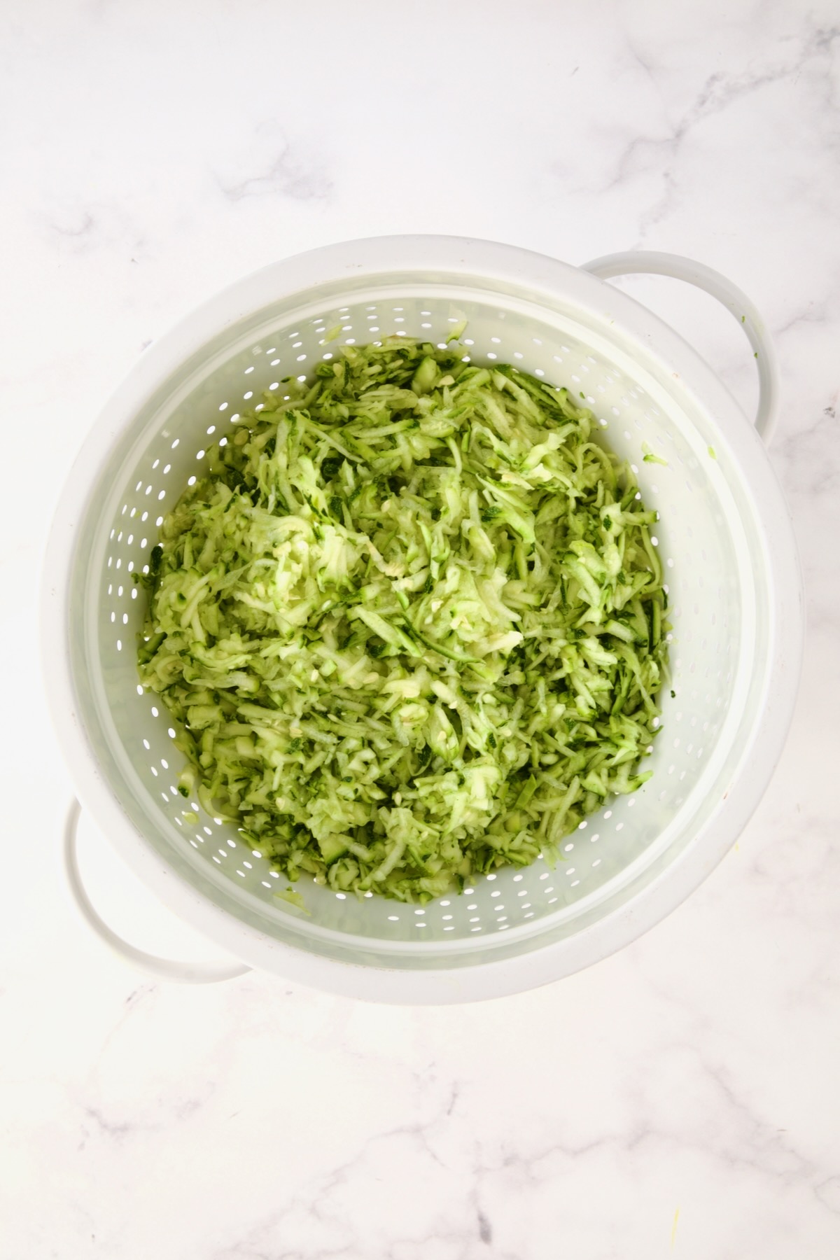Shredded zucchini in white colander.