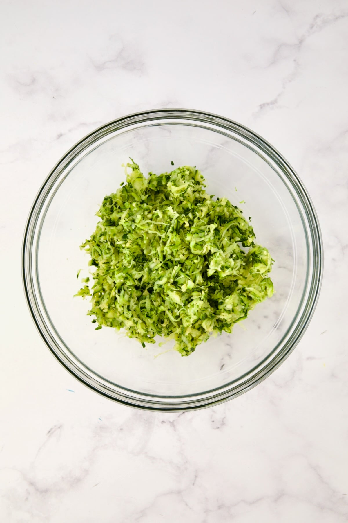 Squeezed shredded zucchini in glass bowl.