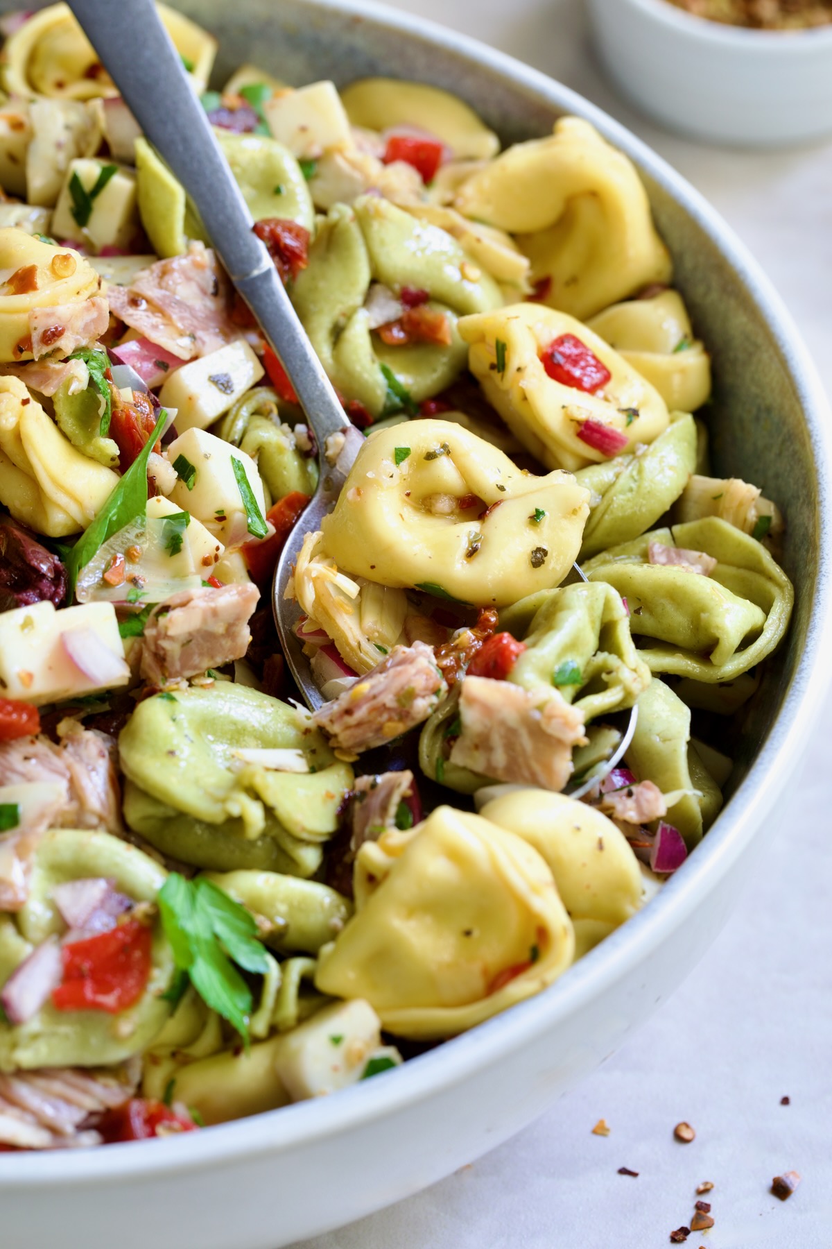 Antipasto Tortellini Salad in serving bowl with serving spoon scooping some up.