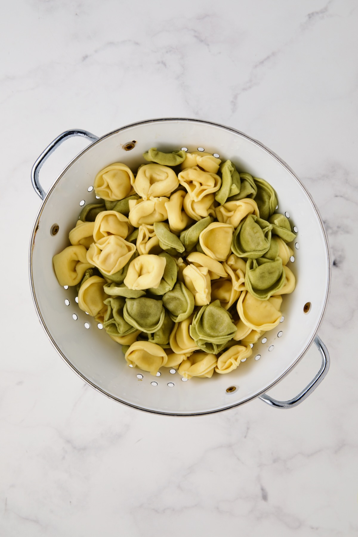 Cooked multi-colored cheese tortellini in white enamel colander.
