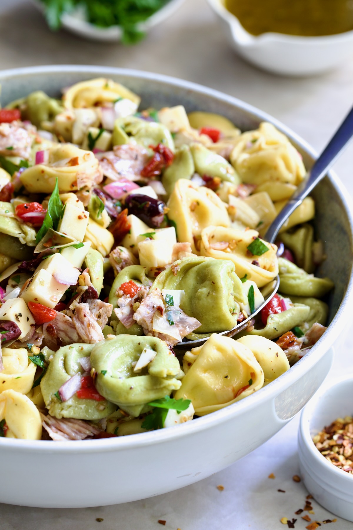 Antipasto Tortellini Salad in serving bowl with serving spoon scooping some up.