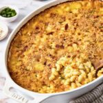 Hatch Green Chili Mac and Cheese in oval baking dish with some being scooped out with wooden spoon.