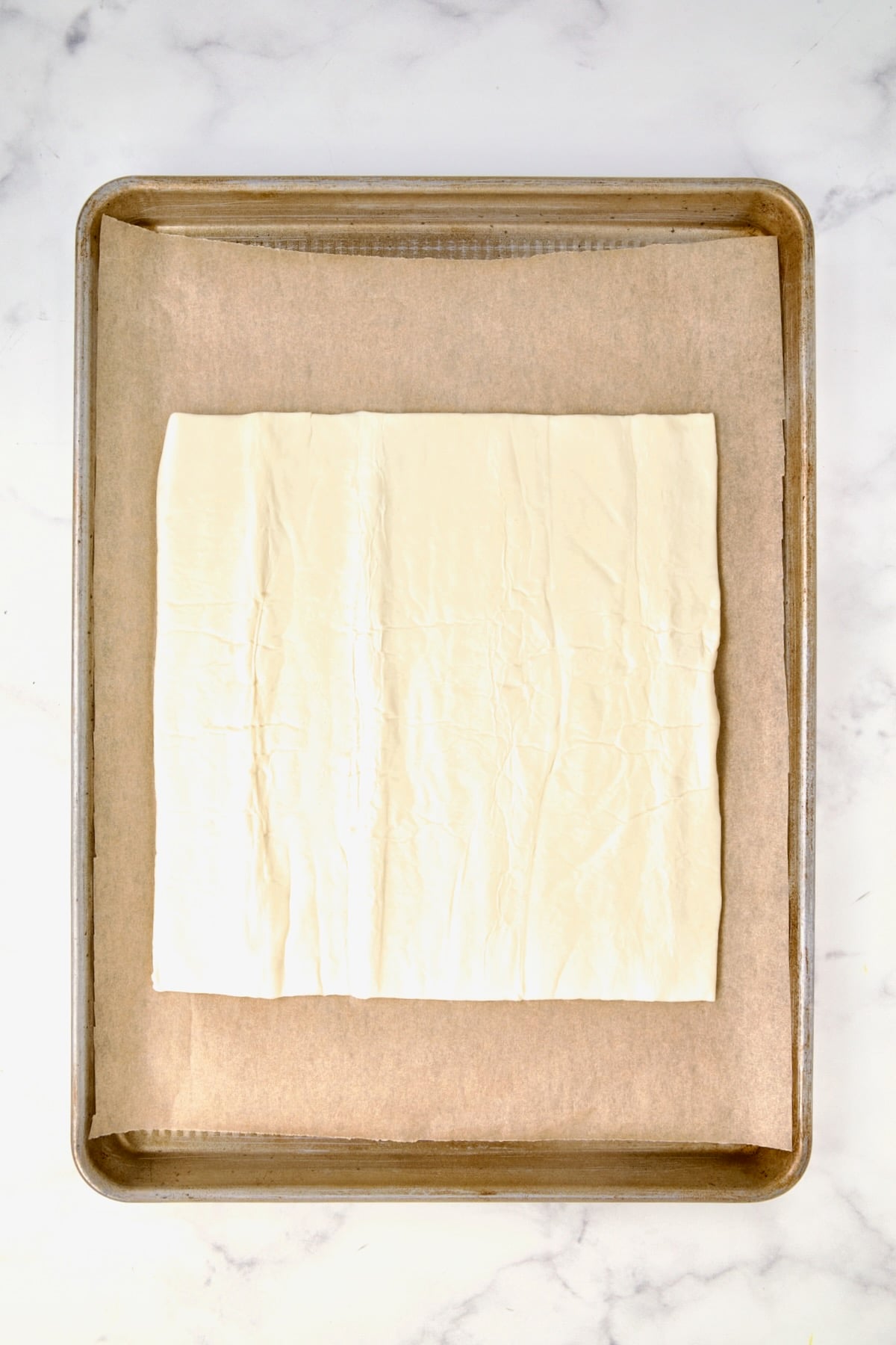 Puff pastry piece on parchment paper-lined rimmed baking sheet.