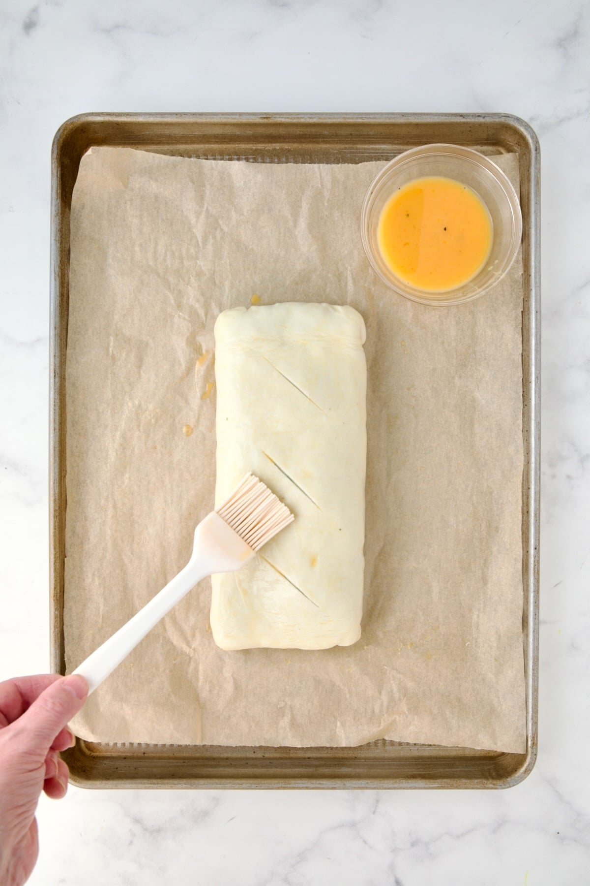 Fully assembled Italian Vegetable Strudel turned over for baking with three slits cut in the top being brushed with egg wash.