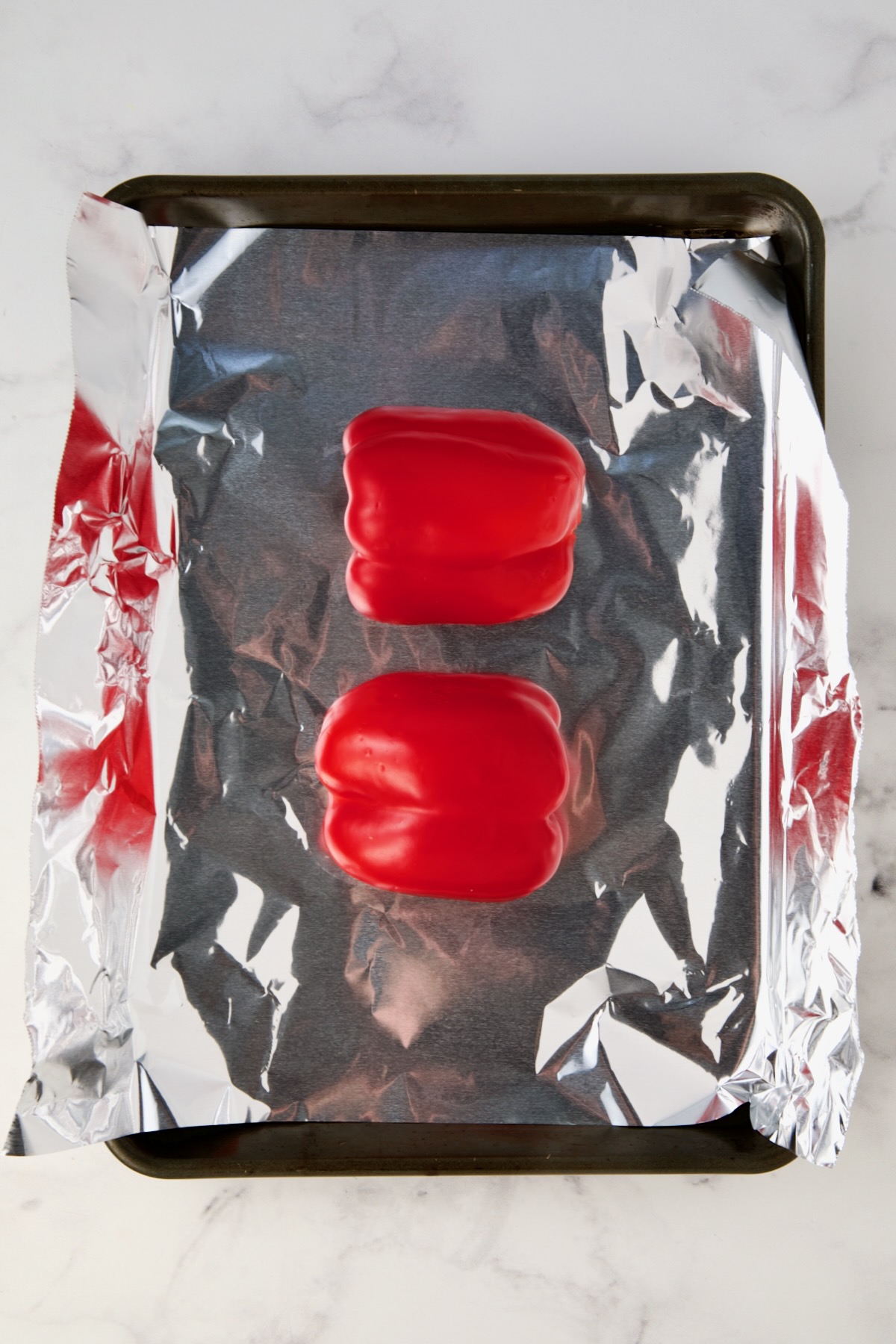 Two red bell pepper halves on aluminum foil-lined rimmed sheet pan before being roasted.