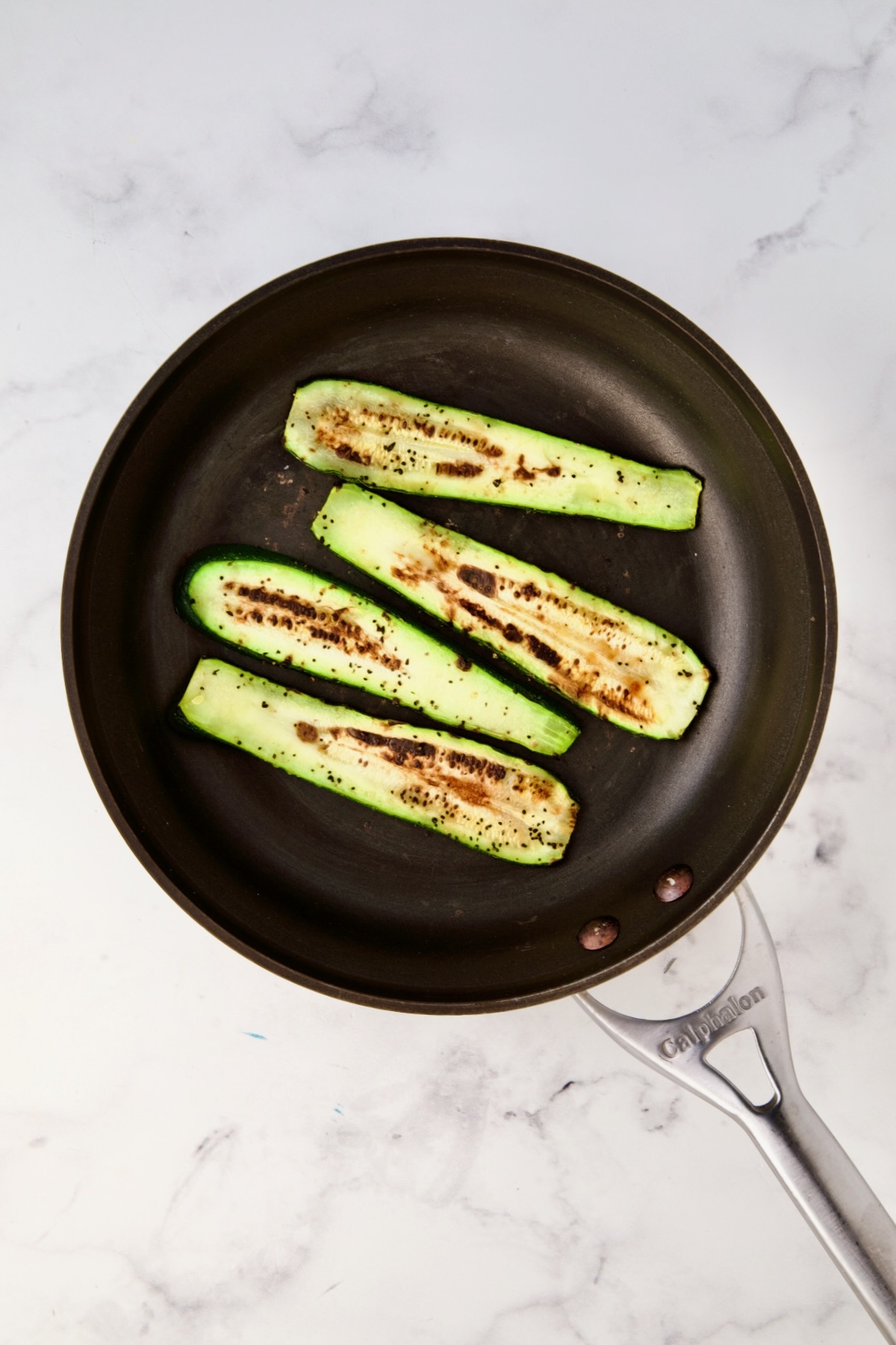 Four charred zucchini slices in nonstick skillet.
