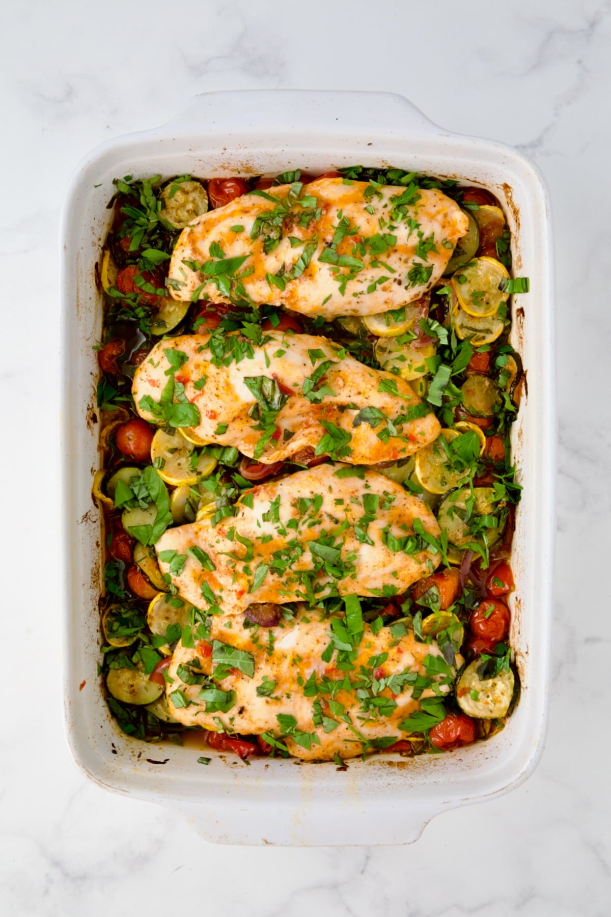 Vegetable and chicken bake in white rectangular baking dish with fresh herbs added.