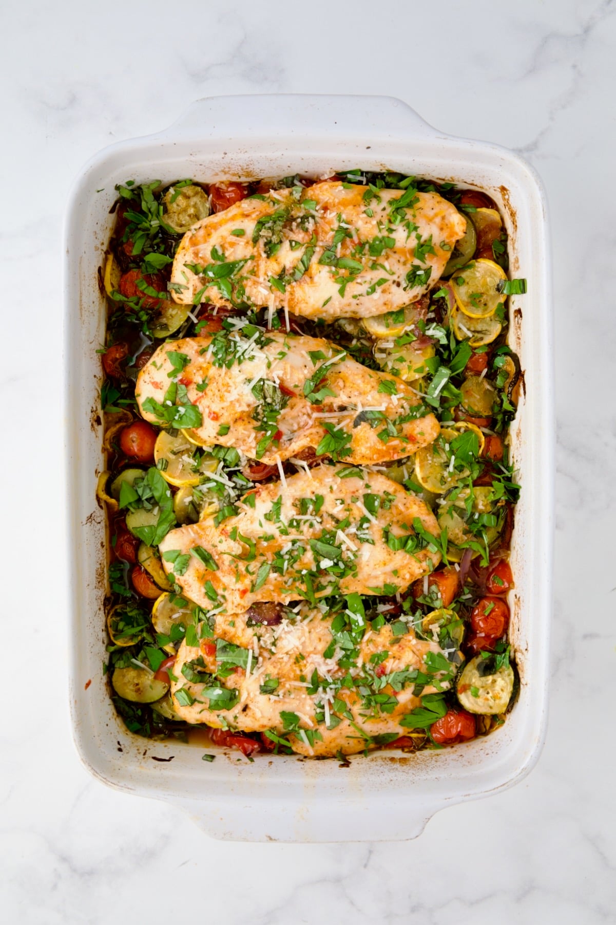 Vegetable and chicken bake in white rectangular baking dish with Parmesan cheese added.