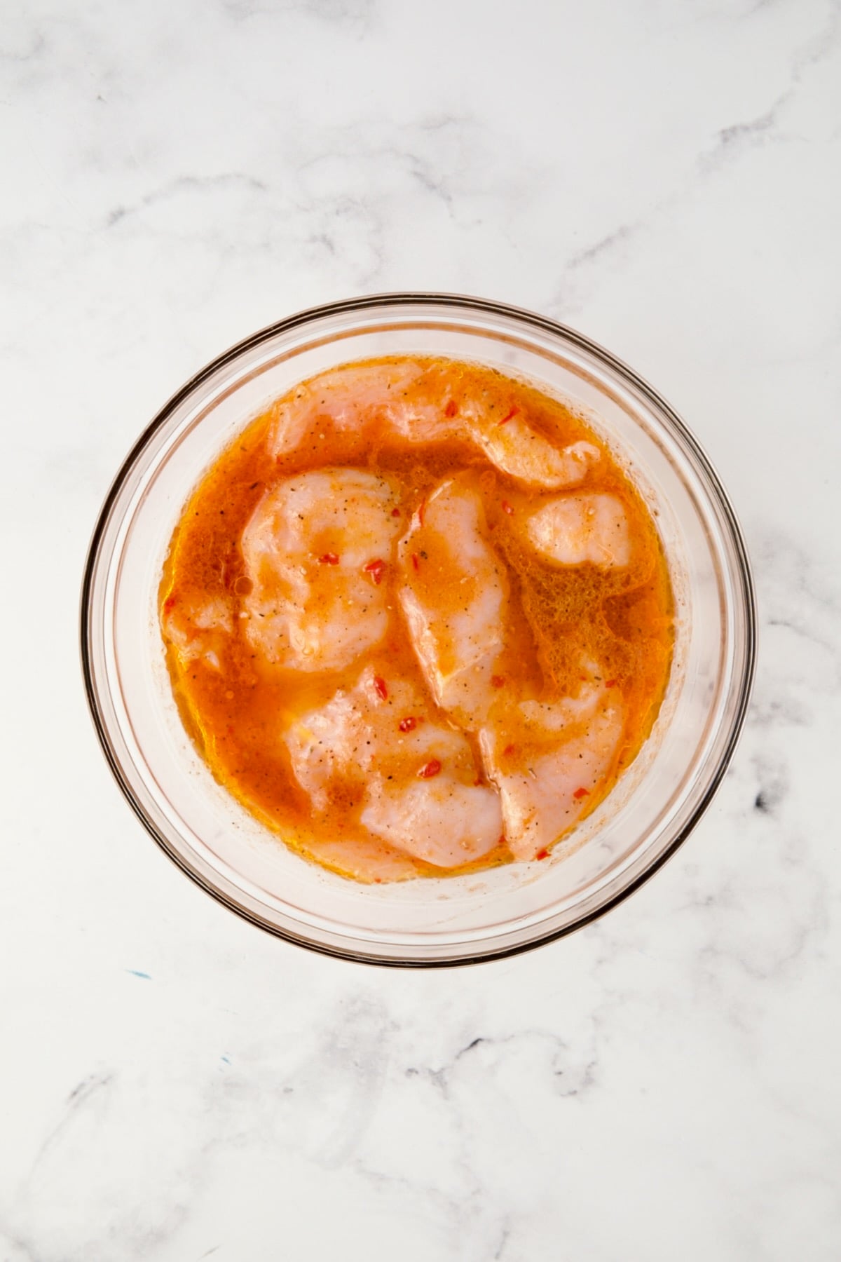 Chicken cutlets in marinade in glass bowl.