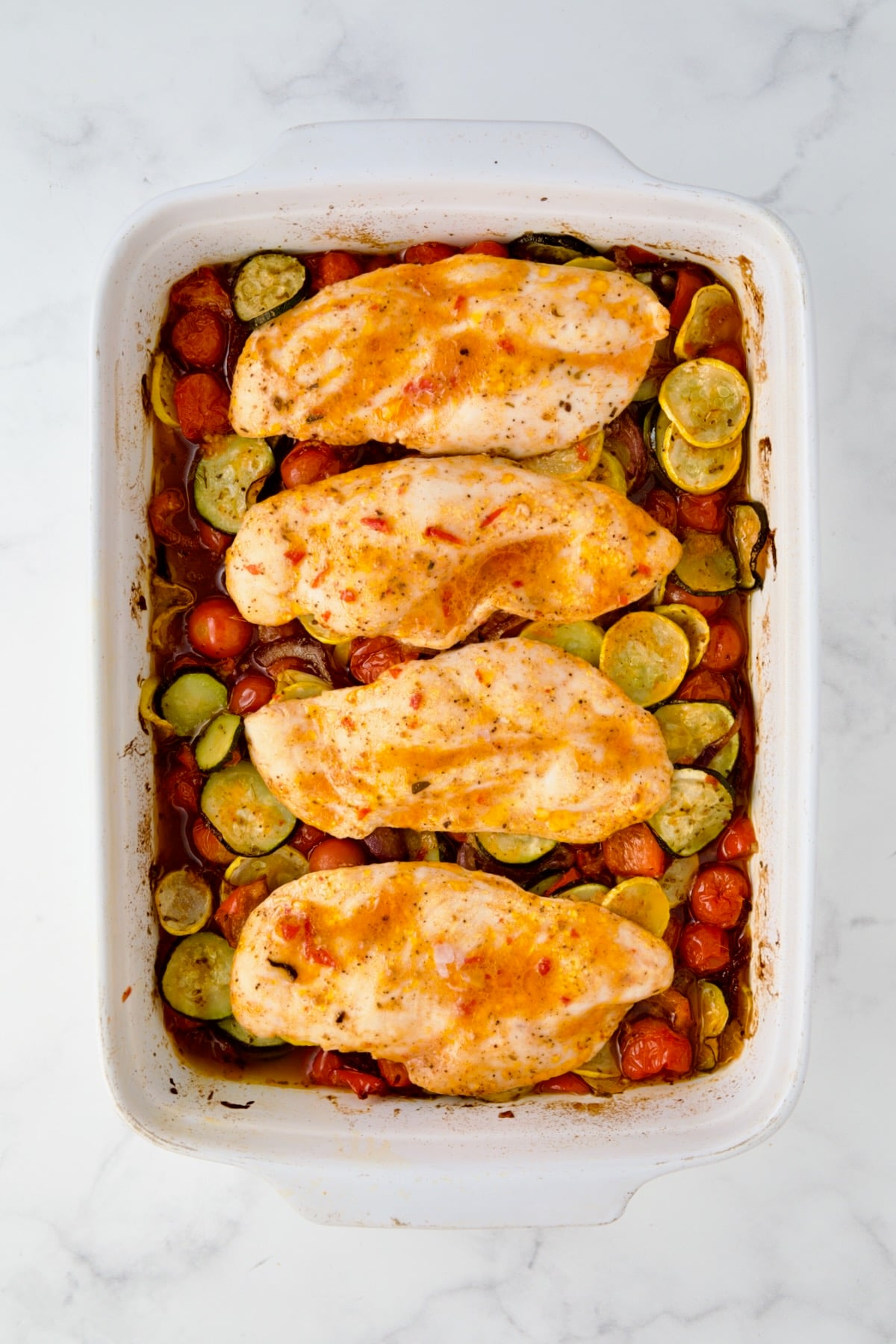 Cooked chicken cutlets and vegetables in white rectangular baking dish.