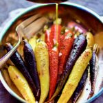 Curry Roasted Carrots in stainless roasting pan with butter being drizzled over.