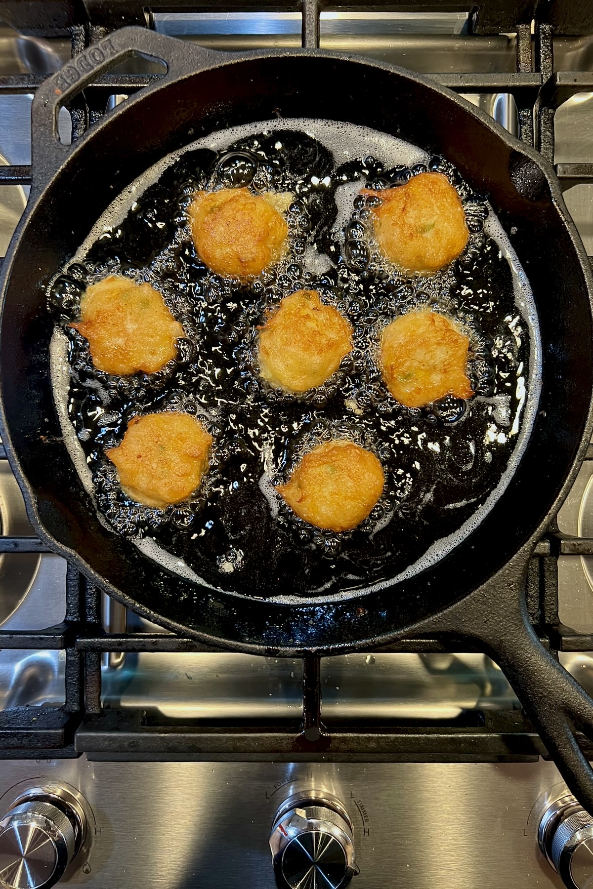 Seven squash puppies frying in a black cast iron skillet.