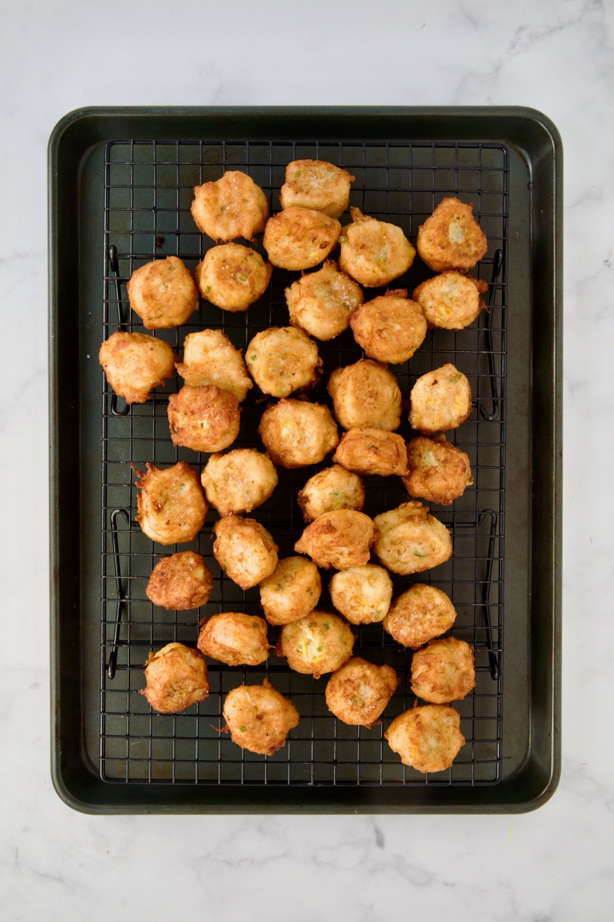 Fried squash puppies on wire rack set over a rimmed sheet pan.
