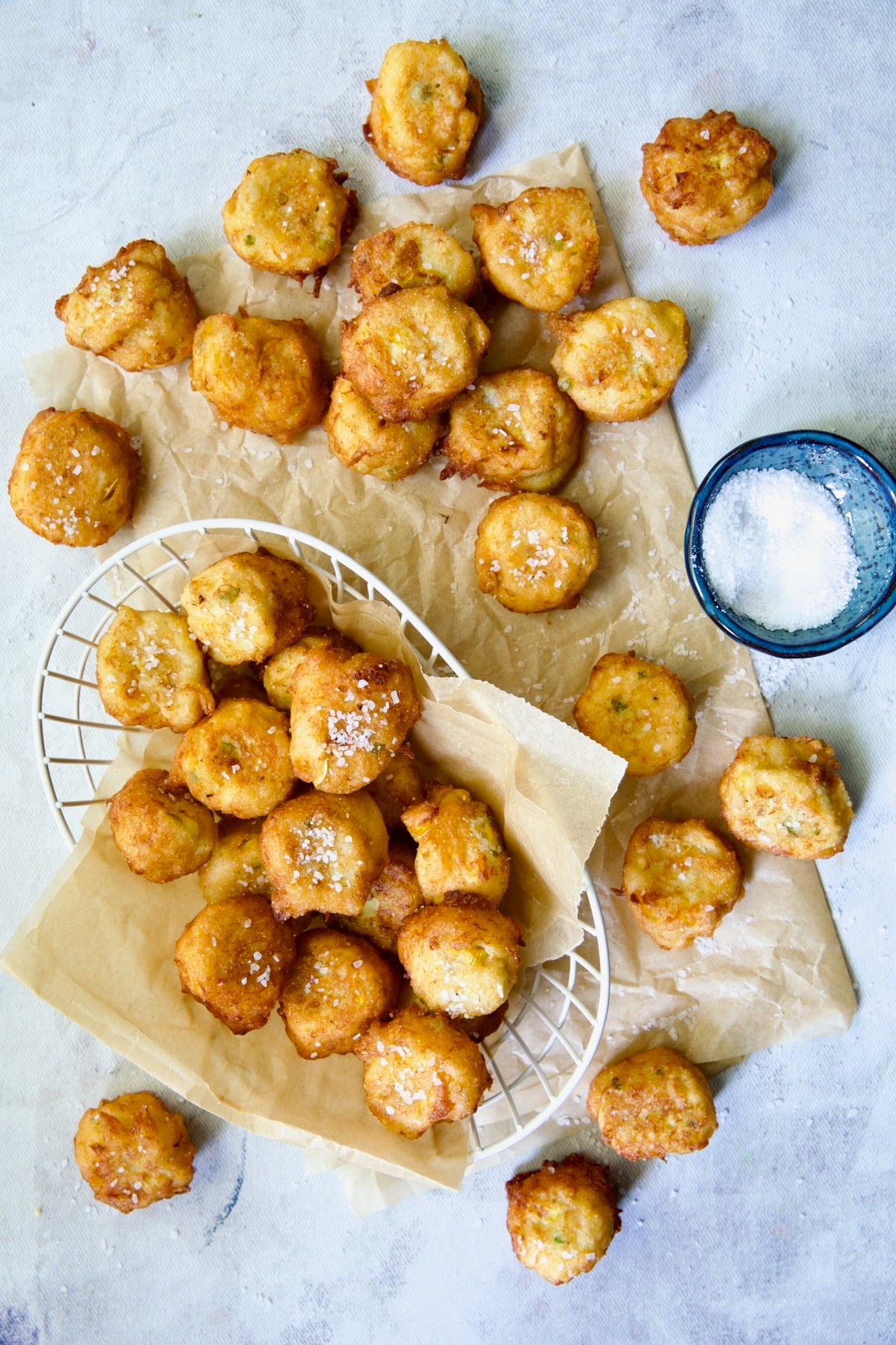 Fried squash puppies on parchment paper with some in a white wire basket.