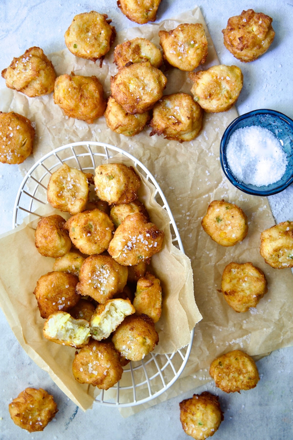 Squash Puppies on parchment paper and in white wire basket with dish of salt.