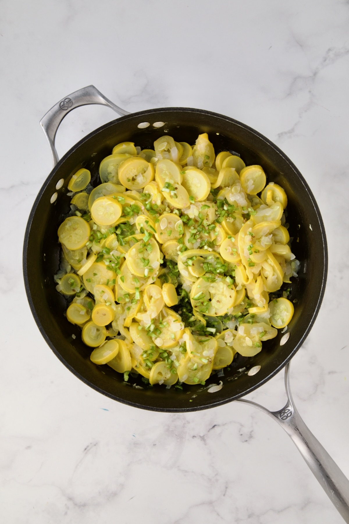 Uncooked sliced yellow squash, chopped onion and diced jalepeno in black skillet.