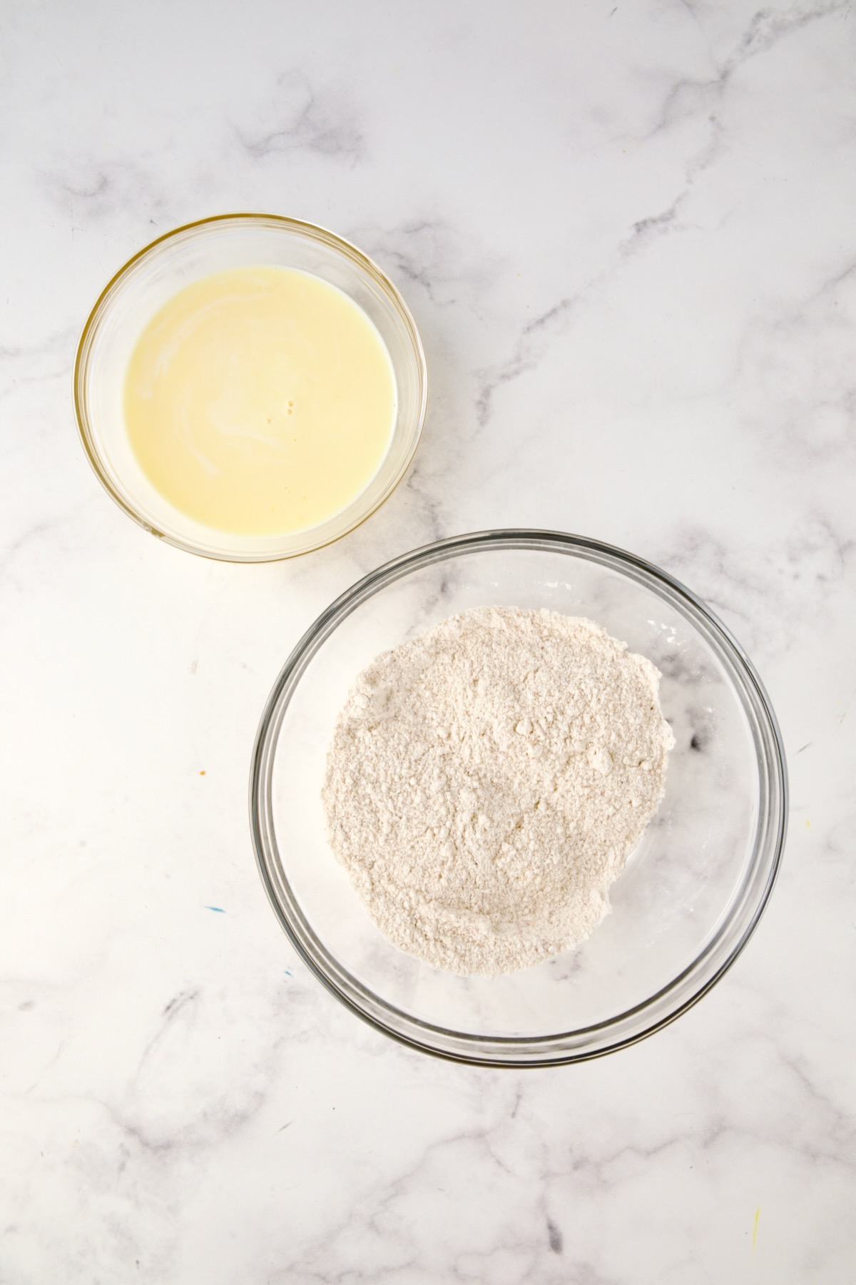 Two glass bowls with buttermilk and egg mixed together in one and cornmeal mix, flour and seasoned salt mixed together in another.