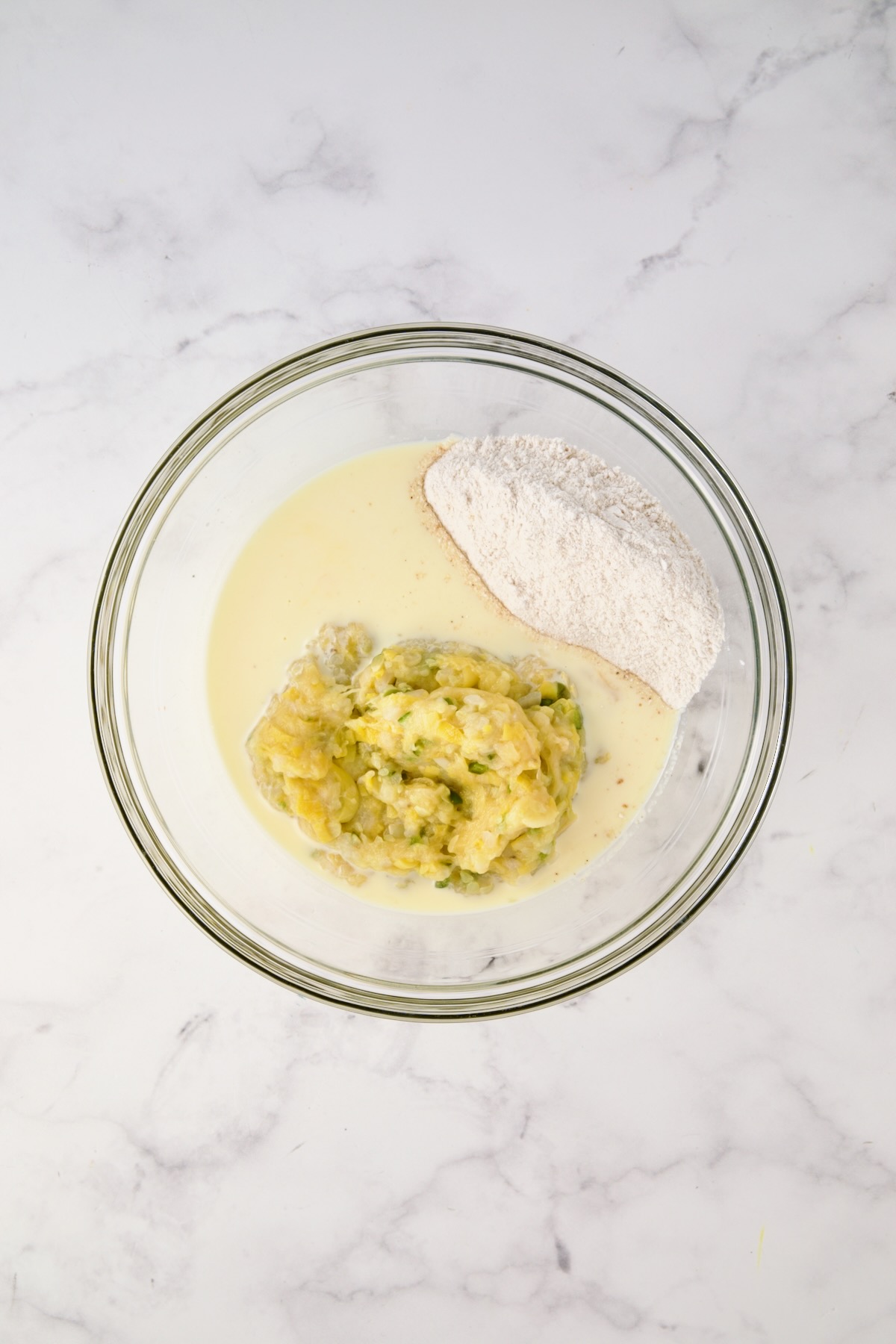 Mashed yellow squash mixture, buttermilk and egg mixture and cornmeal and flour mixture in glass bowl before being mixed together.