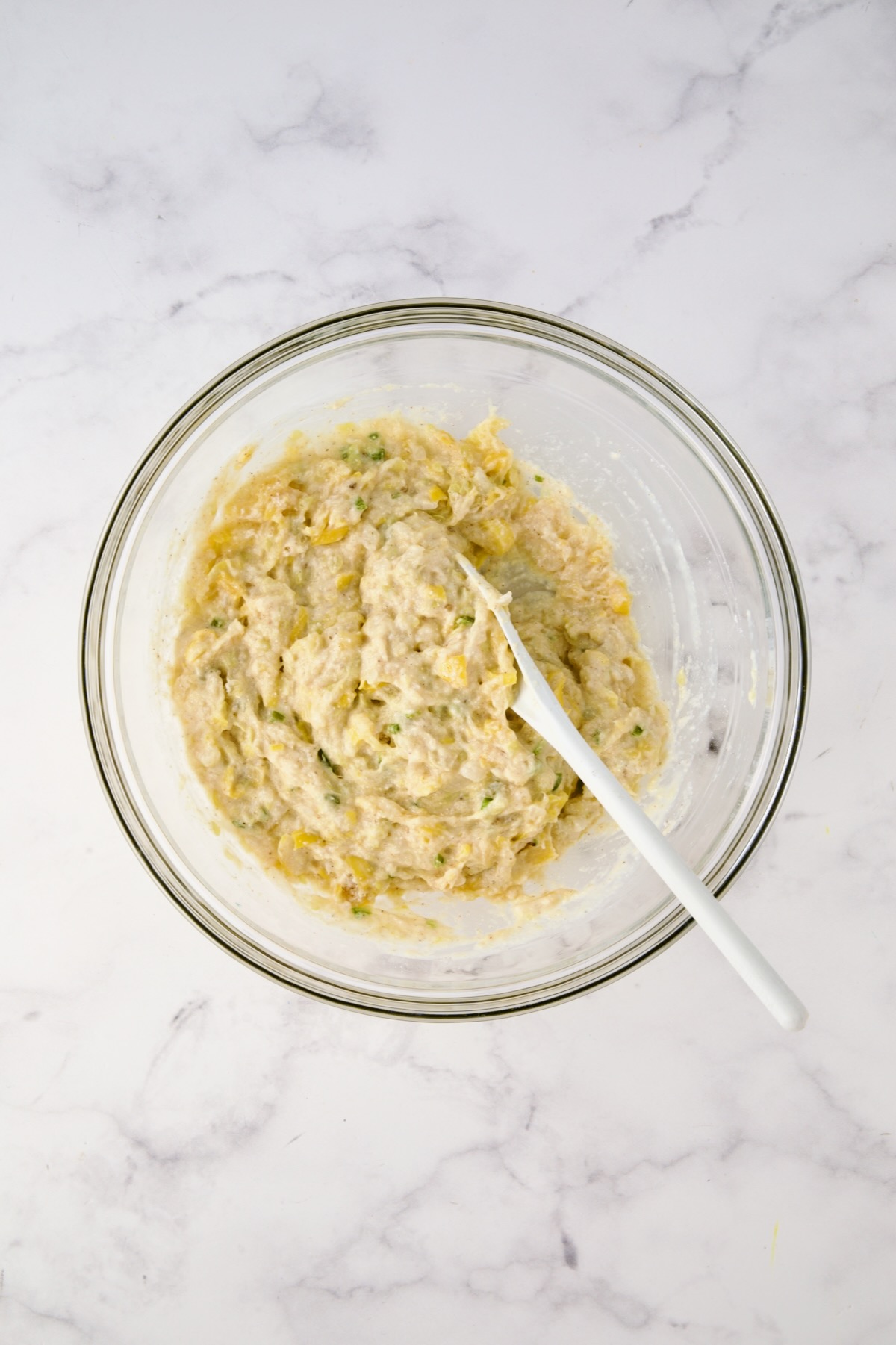 Batter for squash puppies mixed together in glass bowl with white mixing spoon.