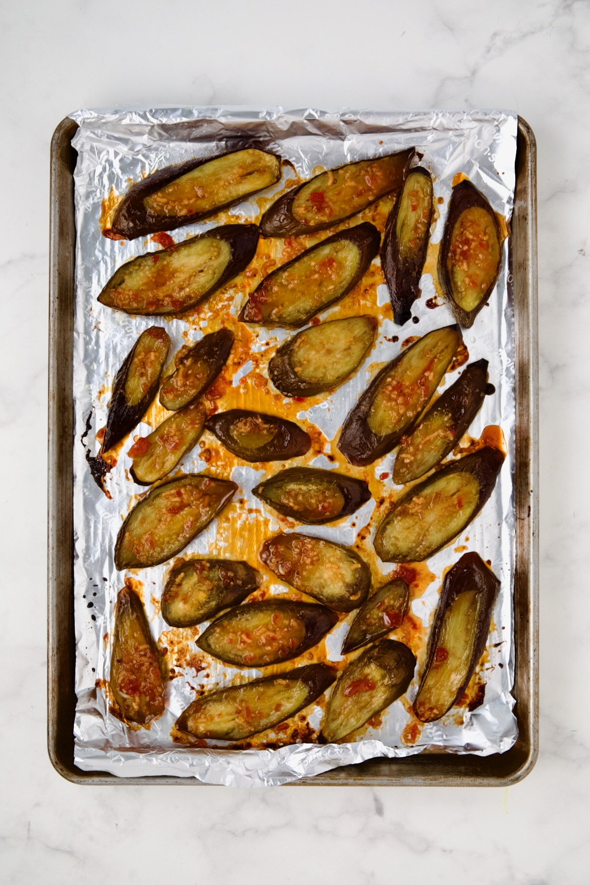 Sliced eggplant on aluminum-foil lined rimmed sheet pan after being broiled.