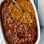 Best Canned Baked Beans Recipe in oval white baking dish with serving spoon.