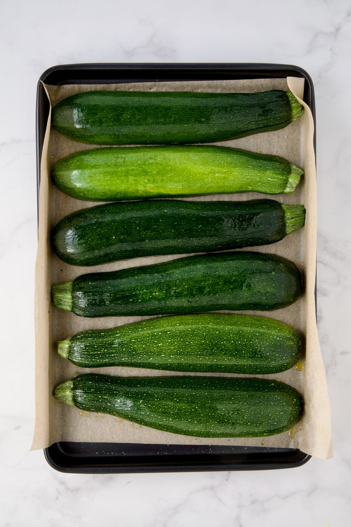 Six zucchini halves on parchment paper-lined rimmed baking sheet.
