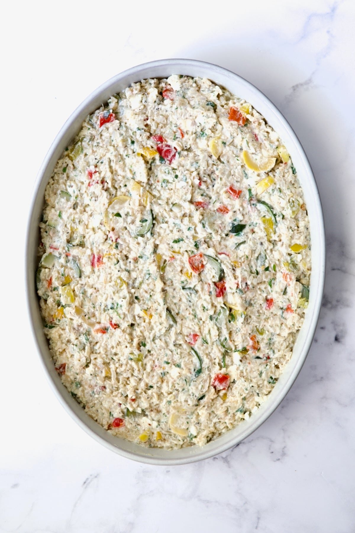 Greek Vegetable Casserole in oval white baking dish before tomatoes and olives go on.