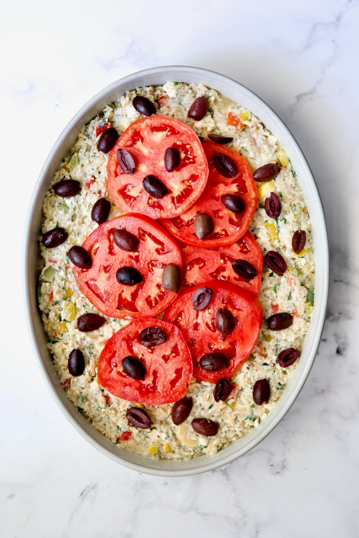 Greek Vegetable Casserole Recipe in oval baking dish with tomatoes and black olives added.